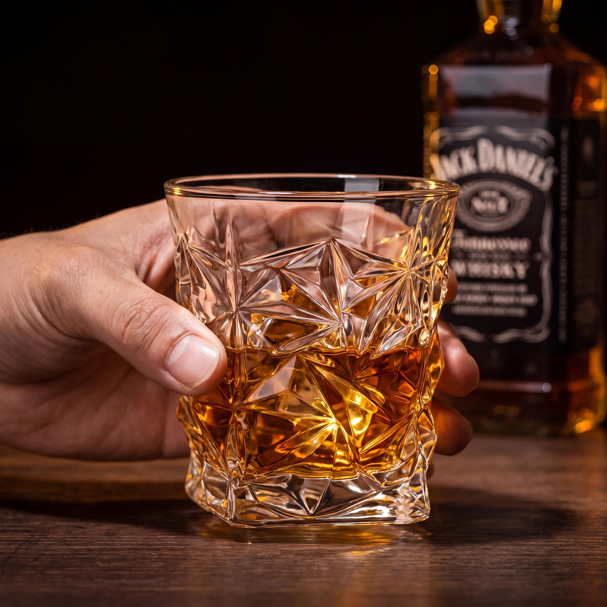 Copo de vidro lapidado geométrico Prisma 290ml com whisky segurado por mão masculina em bar escuro