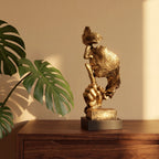 Escultura decorativa Silêncio e Paz dourada em resina sobre aparador de madeira com folha de monstera e luz quente