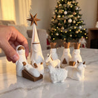 Presépio Sagrada Família 3D com mão posicionando a figura de Maria sobre mármore com árvore de Natal ao fundo