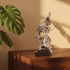 Escultura decorativa Silêncio e Paz prateada em resina sobre aparador de madeira com folha de monstera e luz natural