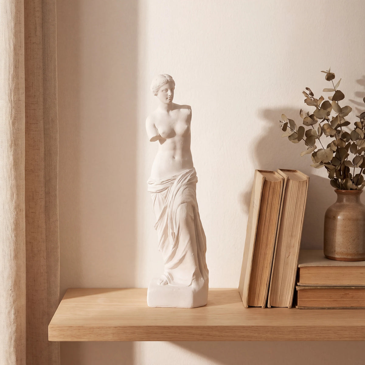 Escultura Vênus de Milo em gesso cru em prateleira de madeira com luz natural suave e cortina de linho