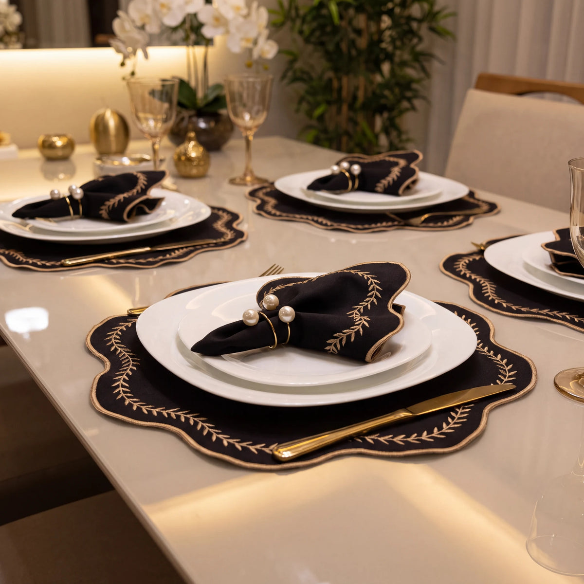 Jogo americano bordado preto e dourado em mesa posta para vários lugares com louça branca e taças
