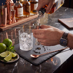 Kit coqueteleira Boston com acessórios de bar sobre tábua de madeira e bancada de mármore