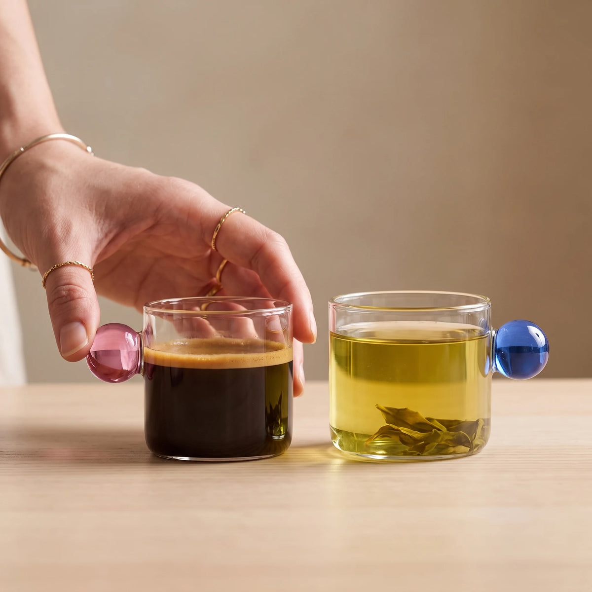 Xícara borossilicato alça rosa com café e xícara alça azul com chá verde, detalhe da bola