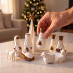 Mão posicionando Rei Mago no presépio Sagrada Família 3D completo sobre mármore branco com luzes de Natal