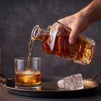 Licoreira de vidro lapidado Âmbar sendo servida, whisky caindo em copo com esfera de gelo, tampa ao lado