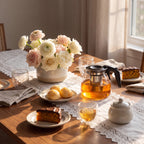 Bule de vidro com infusor em mesa de chá da tarde com pão de queijo e bolo de cenoura