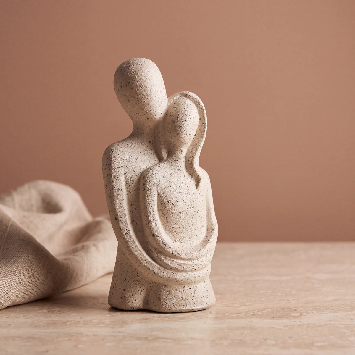 Escultura casal abraçado com fundo terracota e tecido de linho