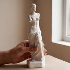 Mão segurando escultura Vênus de Milo em gesso cru mostrando escala compacta de 25cm