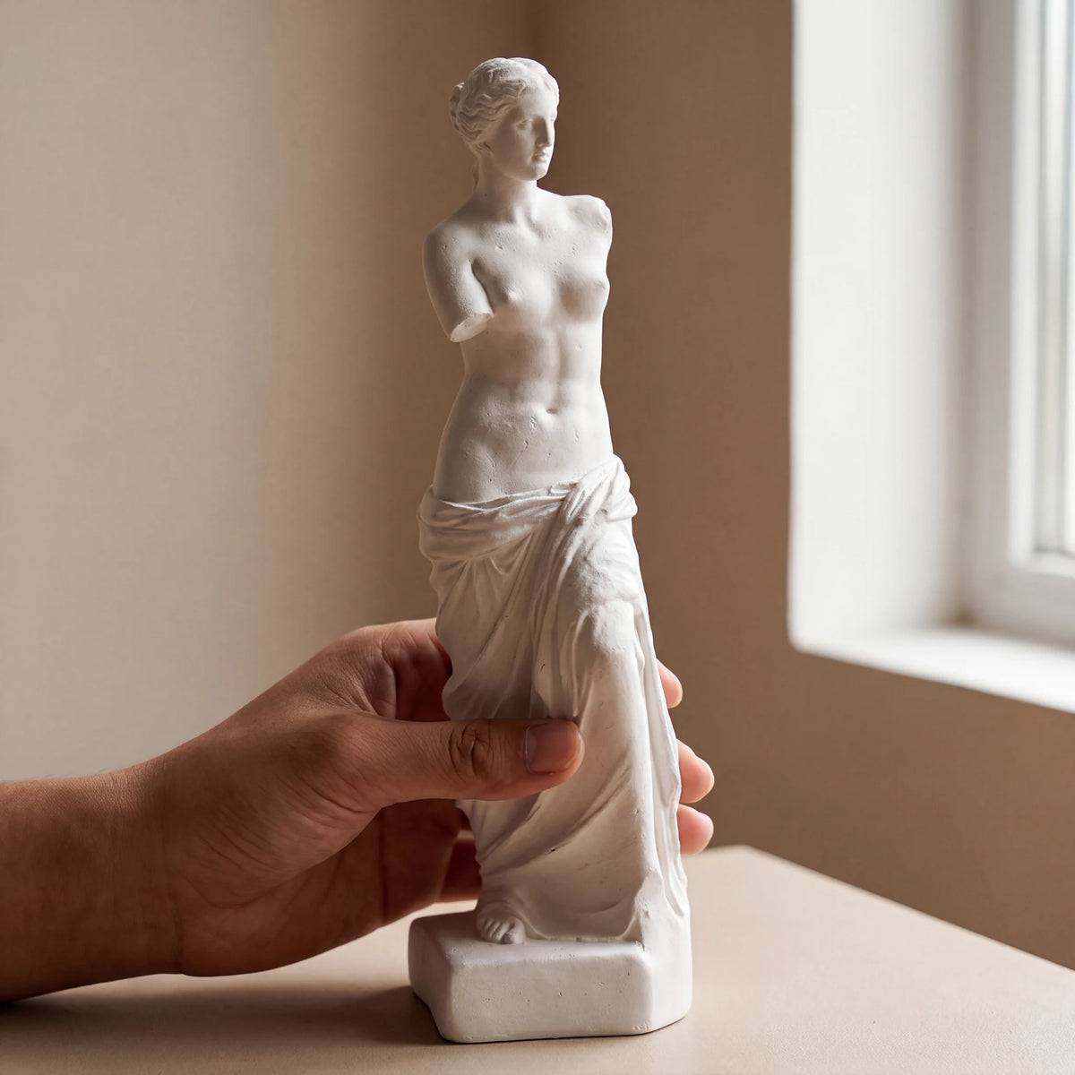 Mão segurando escultura Vênus de Milo em gesso cru mostrando escala compacta de 25cm