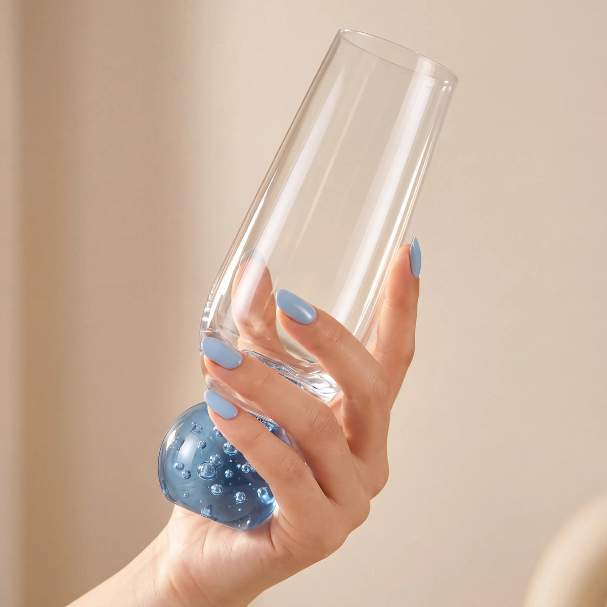 Mão feminina com unhas azuis segurando taça champagne bubble azul pela base esférica com bolhas no vidro
