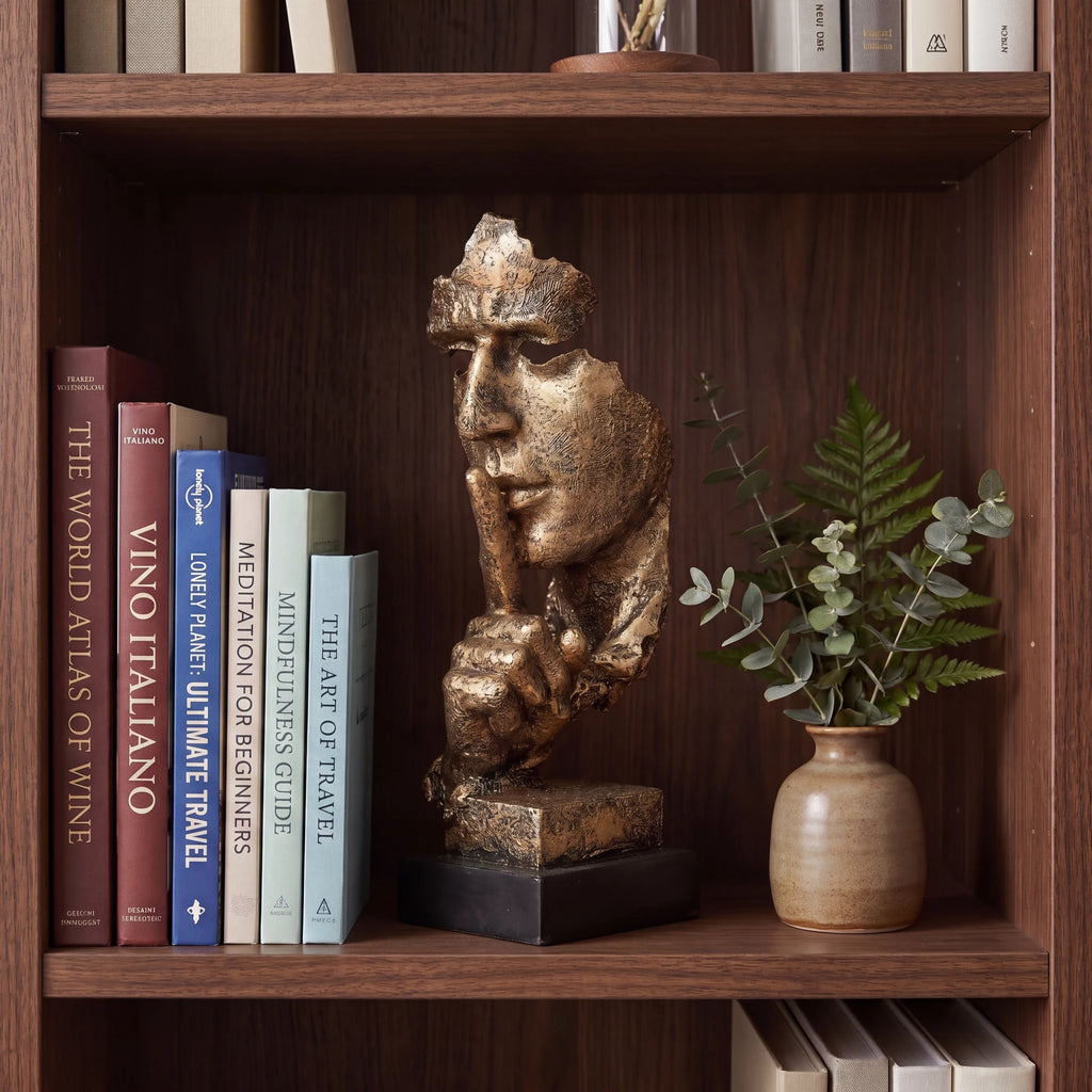 Escultura decorativa Silêncio e Paz dourada em estante de madeira com livros e vaso de eucalipto