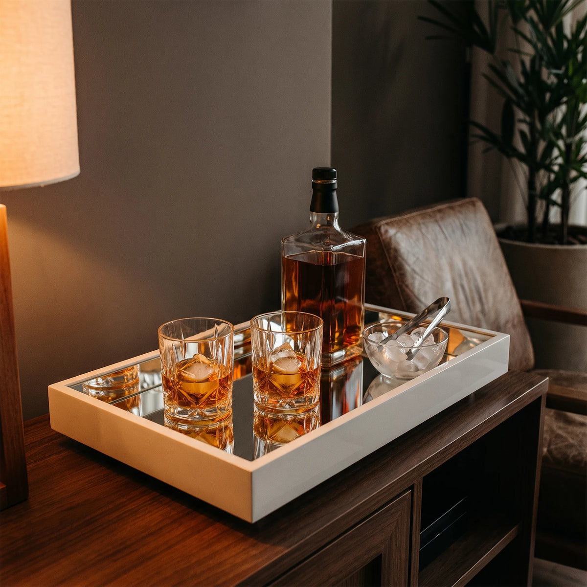 Bandeja espelhada off white com copos de whisky, garrafa e bowl de gelo em aparador de bar com poltrona