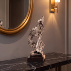 Escultura decorativa Silêncio e Paz prateada sobre console de mármore escuro com espelho dourado e arandela âmbar